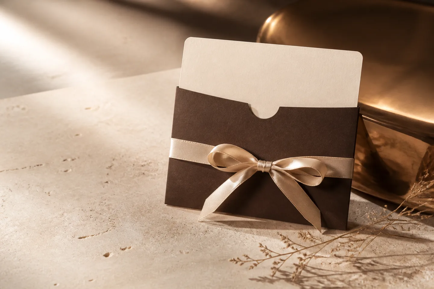 An ivory gift card presented in an espresso sleeve with champagne ribbon